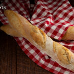 Photo of two baguettes sitting on a red gingham towel. The Clair Obscur: Expedition 33 logos is in the top left.